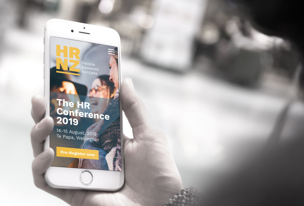 HRNZ-conference-web-mobile-woman-v2_cropped Hand holding a mobile phone showing a mobile optimised website by brand consultants Wonderlab.