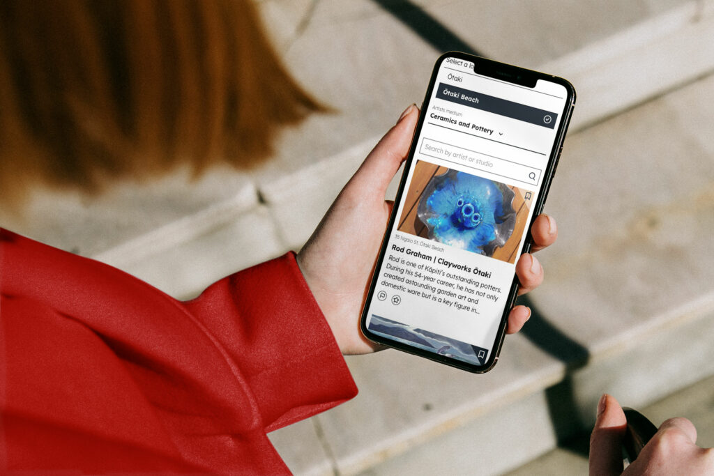 kcat-mobile-artistlist A woman holding a phone with an article on it.