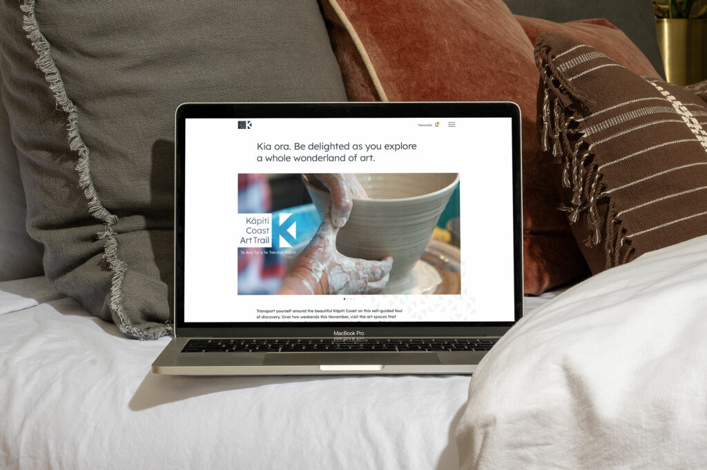 kcat_web-home A laptop is on a bed with pillows and pillows.