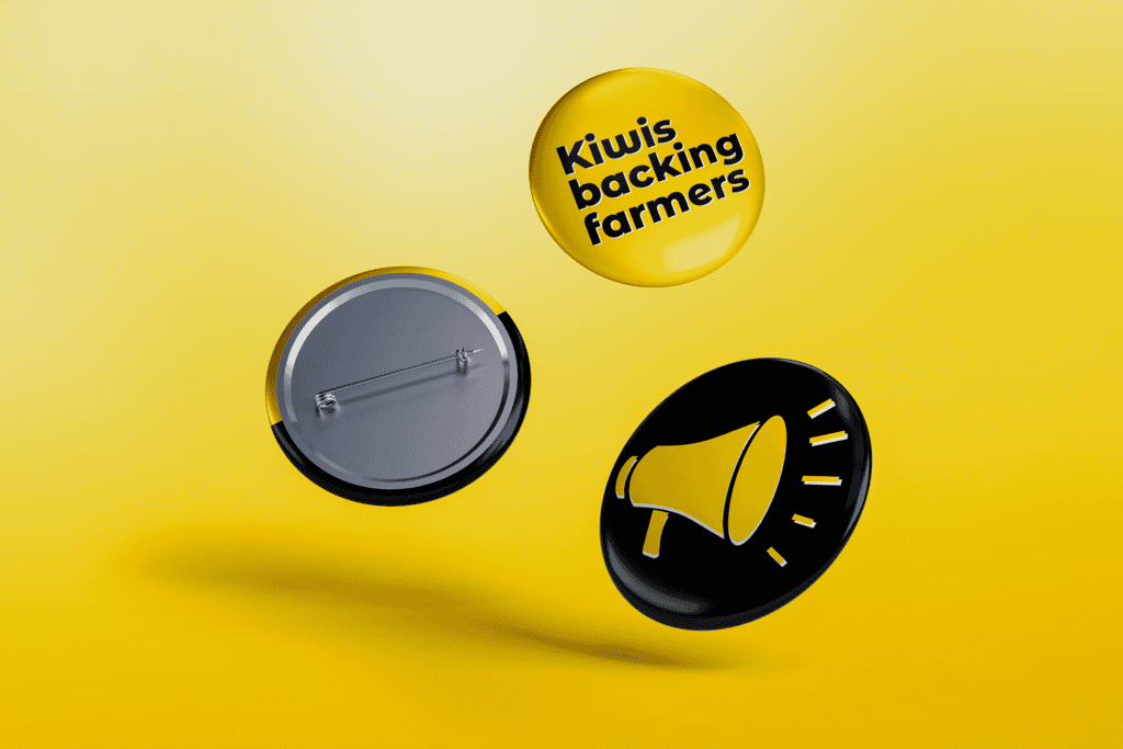 BeefandLamb_Pins Three buttons drifting mid-air against a yellow background. One button shows the message "Kiwis backing farmers" in black text on a yellow background. Another button features a yellow megaphone graphic on a black background, while the third button displays its pin-back.