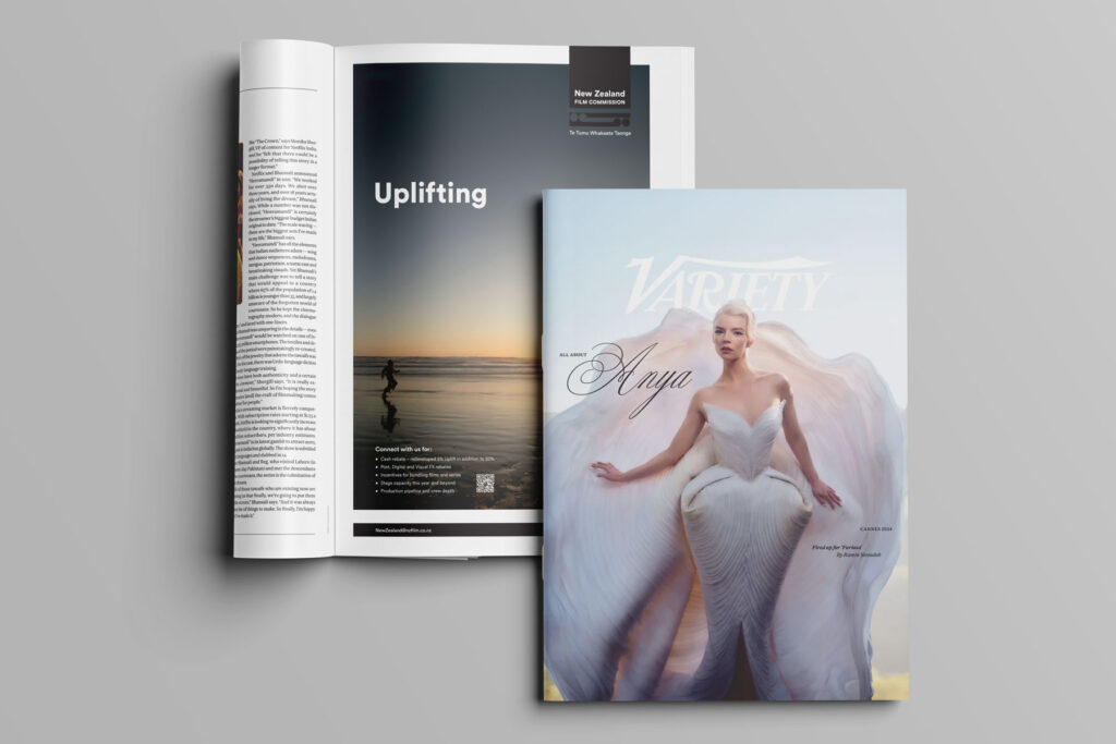 Cannes-Variety-advert-NZFilmCommission1 Open magazine shows an ad with "Uplifting" and a scenic view. On top, a closed Variety magazine features a person in an elegant, flowing white outfit with text "Anya." The background is a soft gradient.
