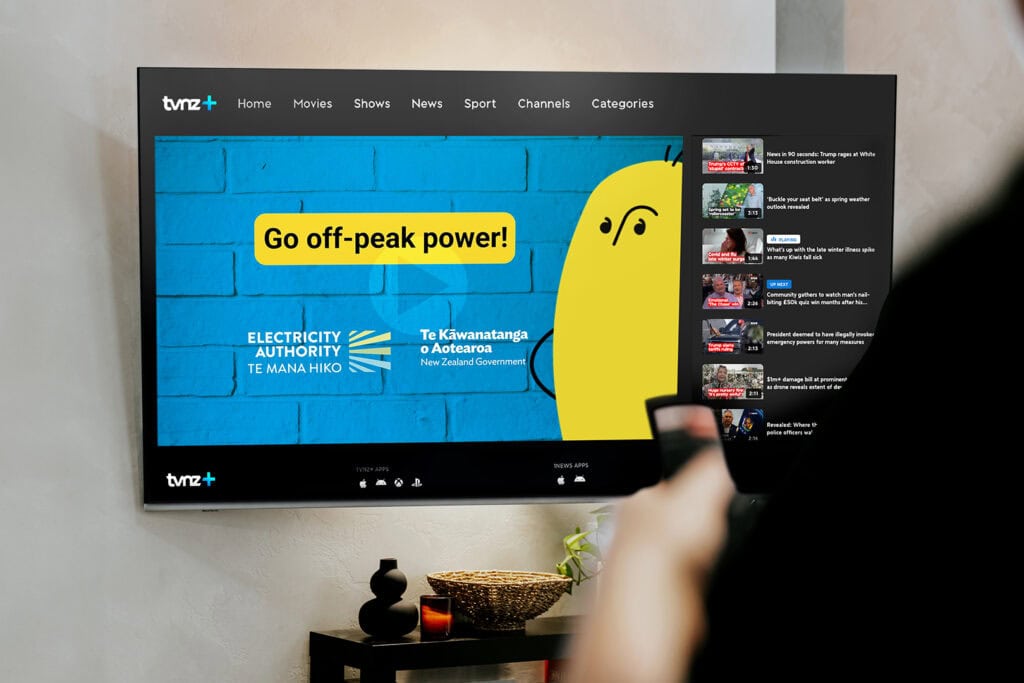 TVNZ+ Campaign ads A TV screen displays a TVNZ+ streaming app with a blue and yellow ad saying "Go off-peak power!" from the Electricity Authority of New Zealand. A person holds a remote, preparing to select content.