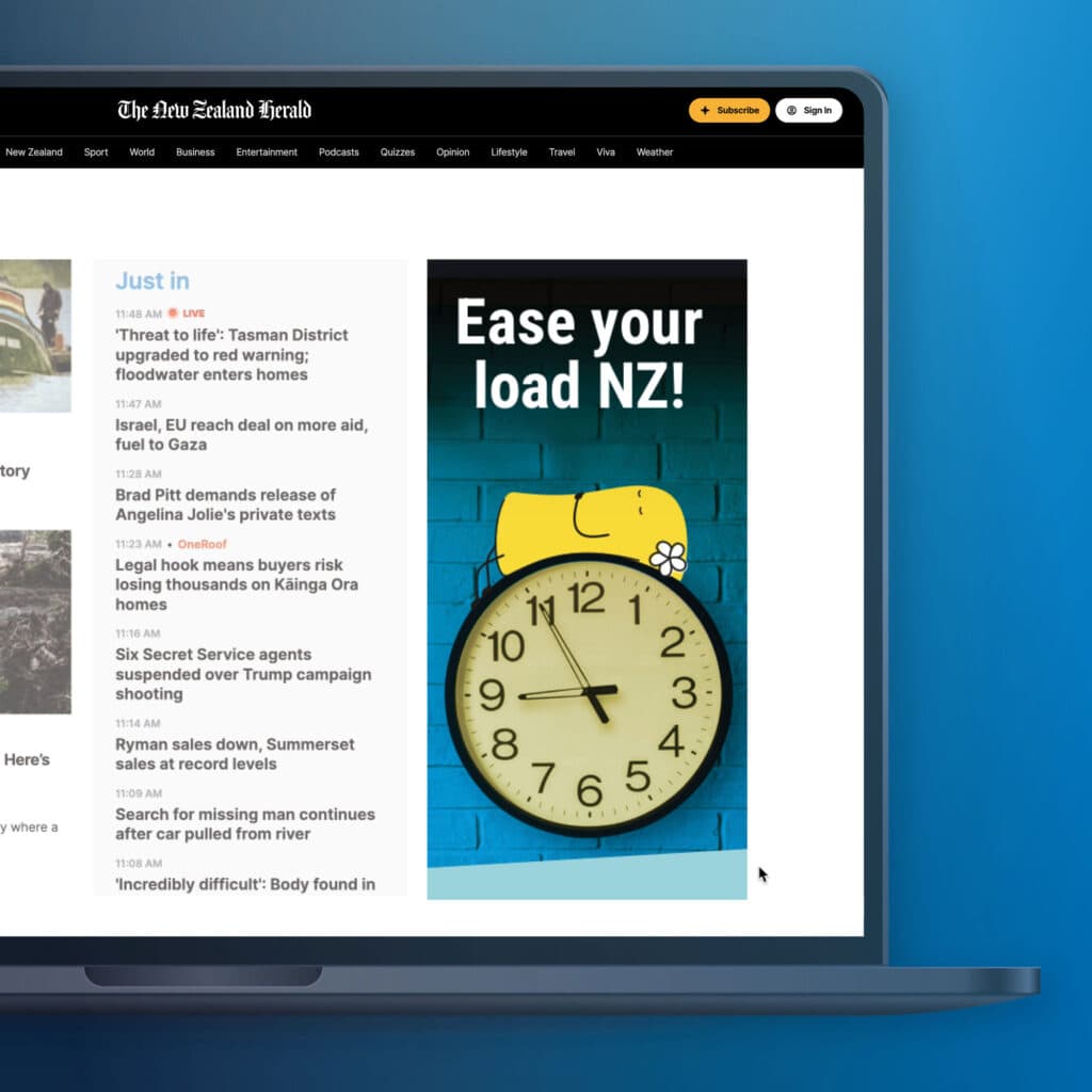 EA-TOU-NZ-Herald-WL A laptop displays The New Zealand Herald website, featuring news headlines on the left and a blue advertisement on the right showing a yellow hand holding a large wall clock with the text "Ease your load NZ!.