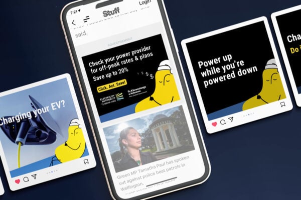 EA-TOU-Social-powerup-powerdown-WL A smartphone displays a news website with a headline about an MP, surrounded by cards featuring illustrations of a yellow character promoting power-saving tips and an image of an electric vehicle charging.